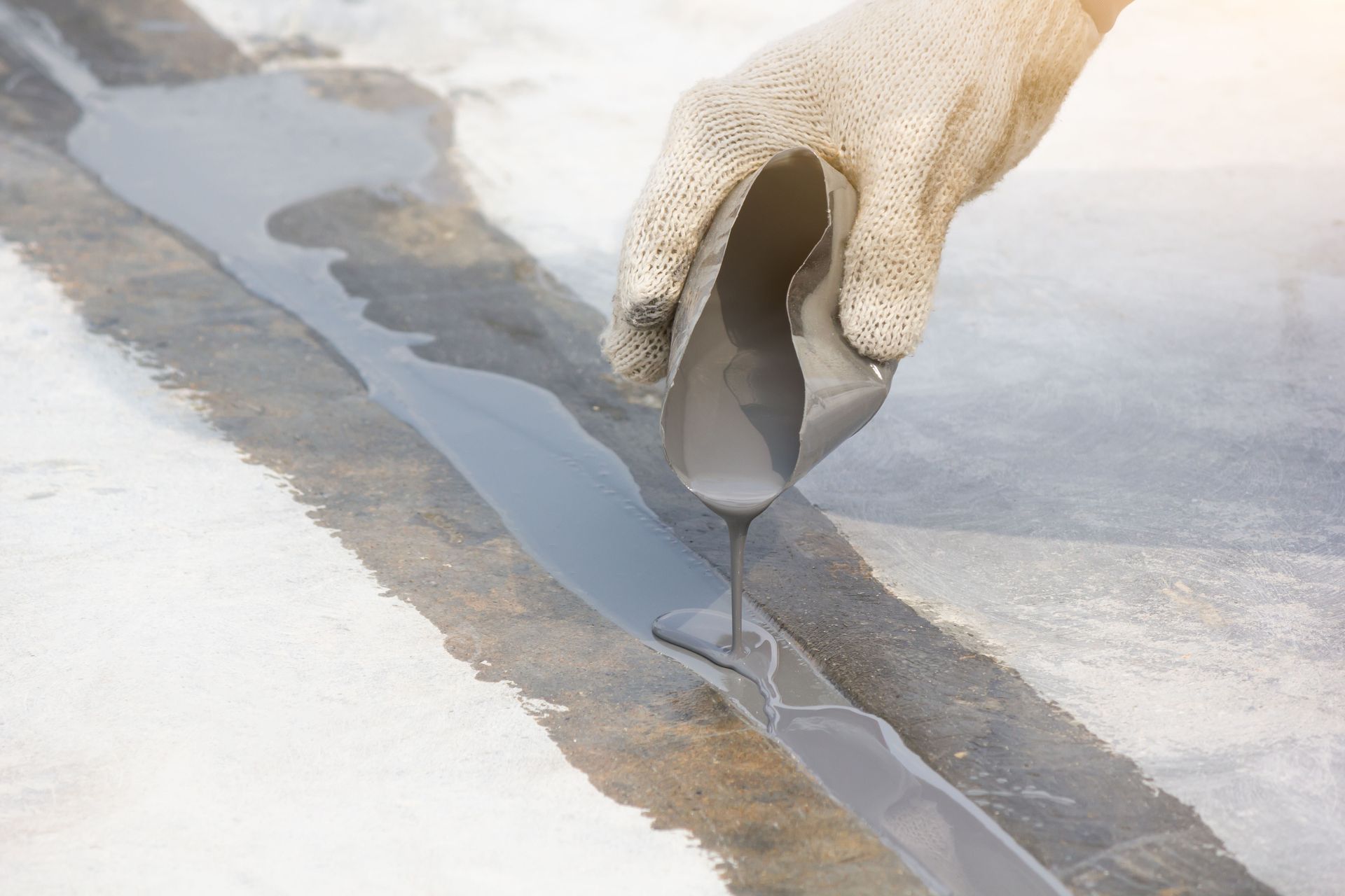 Gloved hand pours liquid along a crack in a concrete floor to seal it