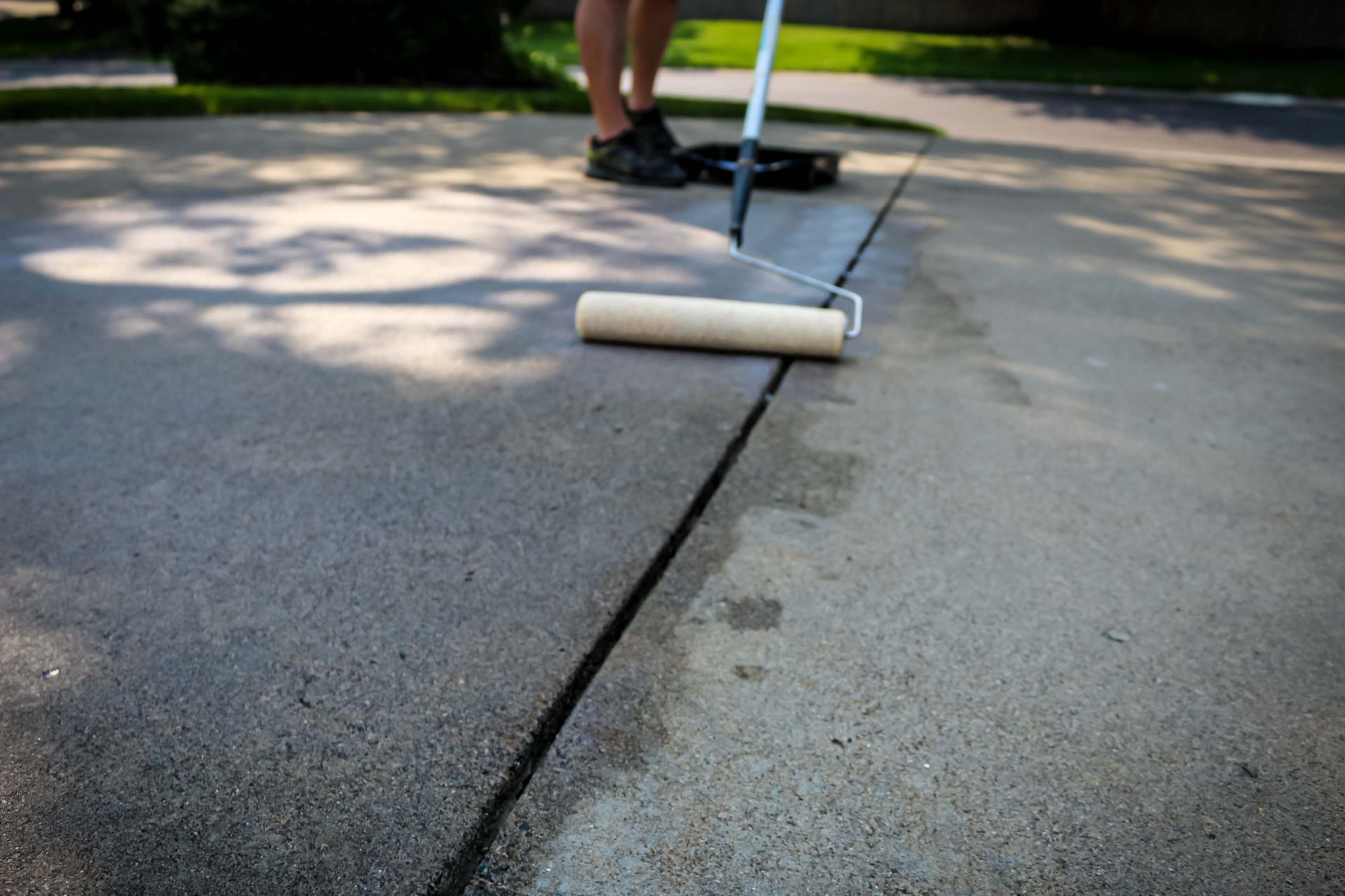 Person rolling gray sealant along a concrete driveway crack