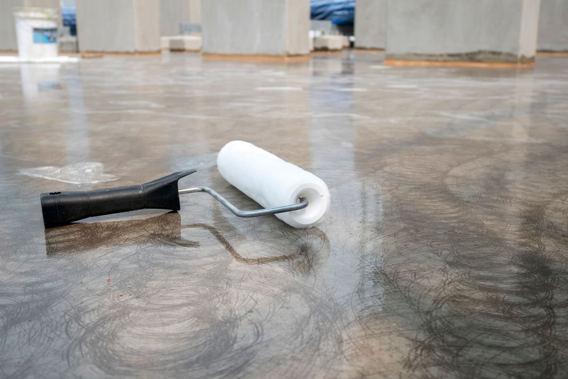White paint roller on wet concrete floor with reflections in an industrial space
