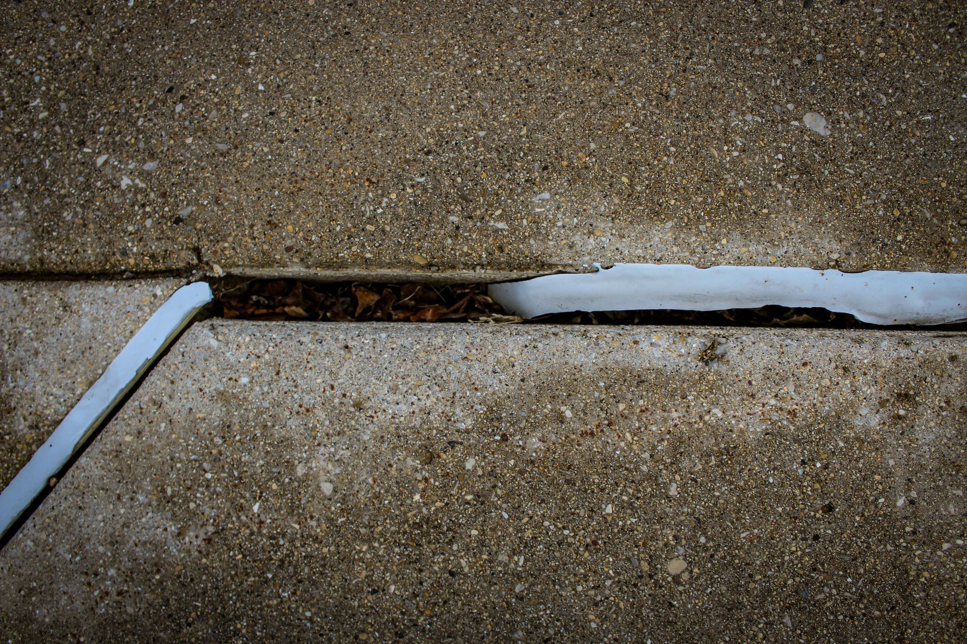 Cracked concrete sidewalk with a long gap filled by dark soil and broken white edges