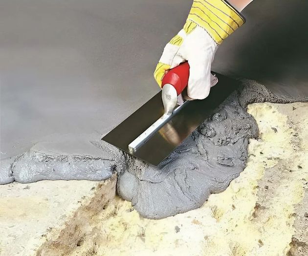 Gloved hand smoothing wet concrete with a trowel on a freshly patched floor