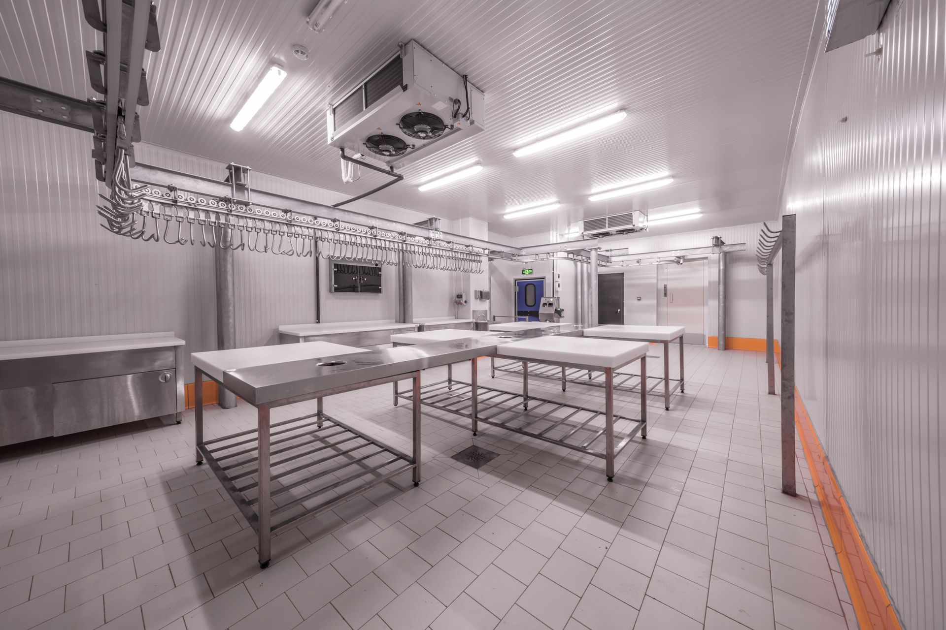 Empty stainless-steel commercial kitchen with prep tables, tiled floor, and overhead lights