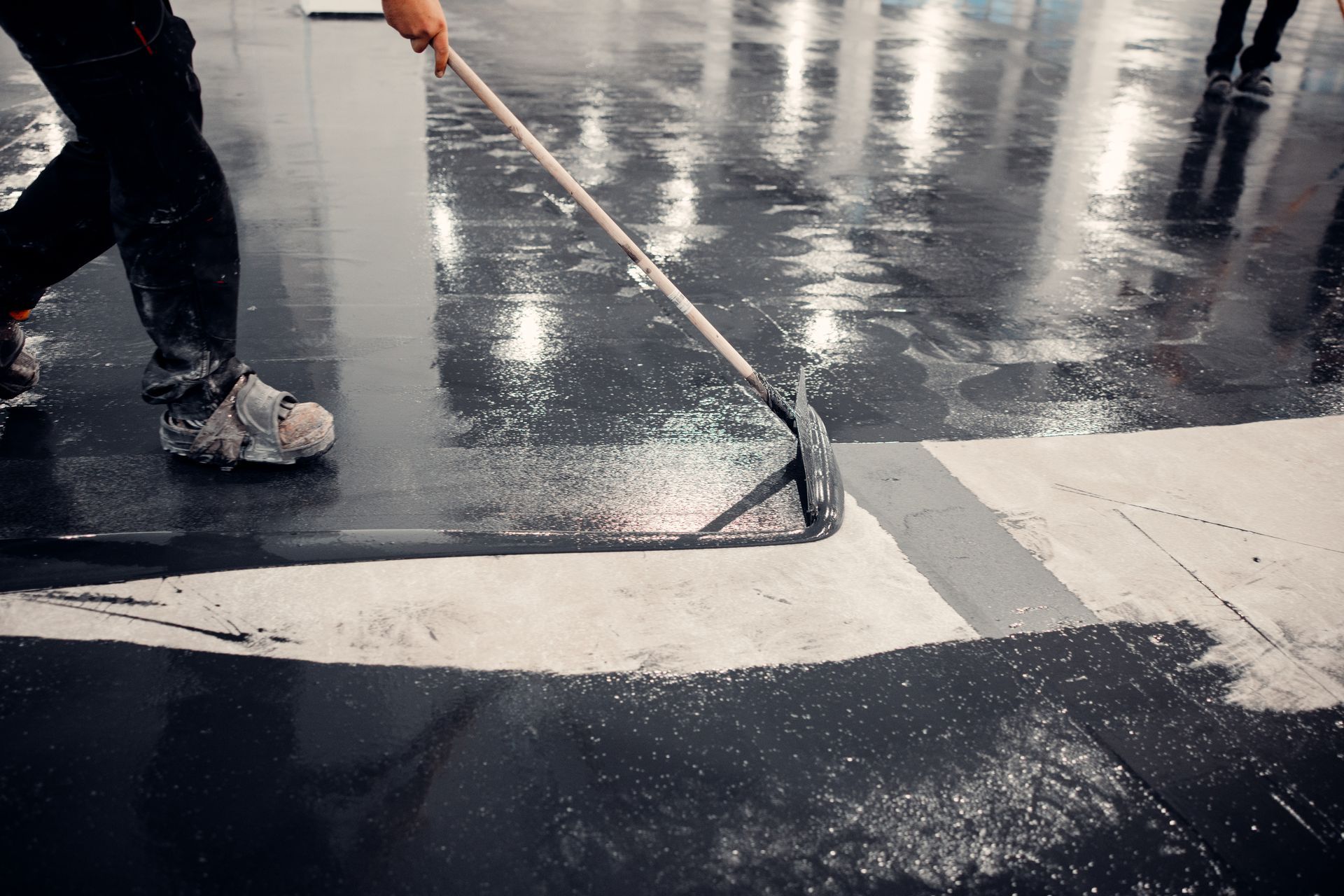 Worker painting white road markings on a wet black pavement with a roller brush
