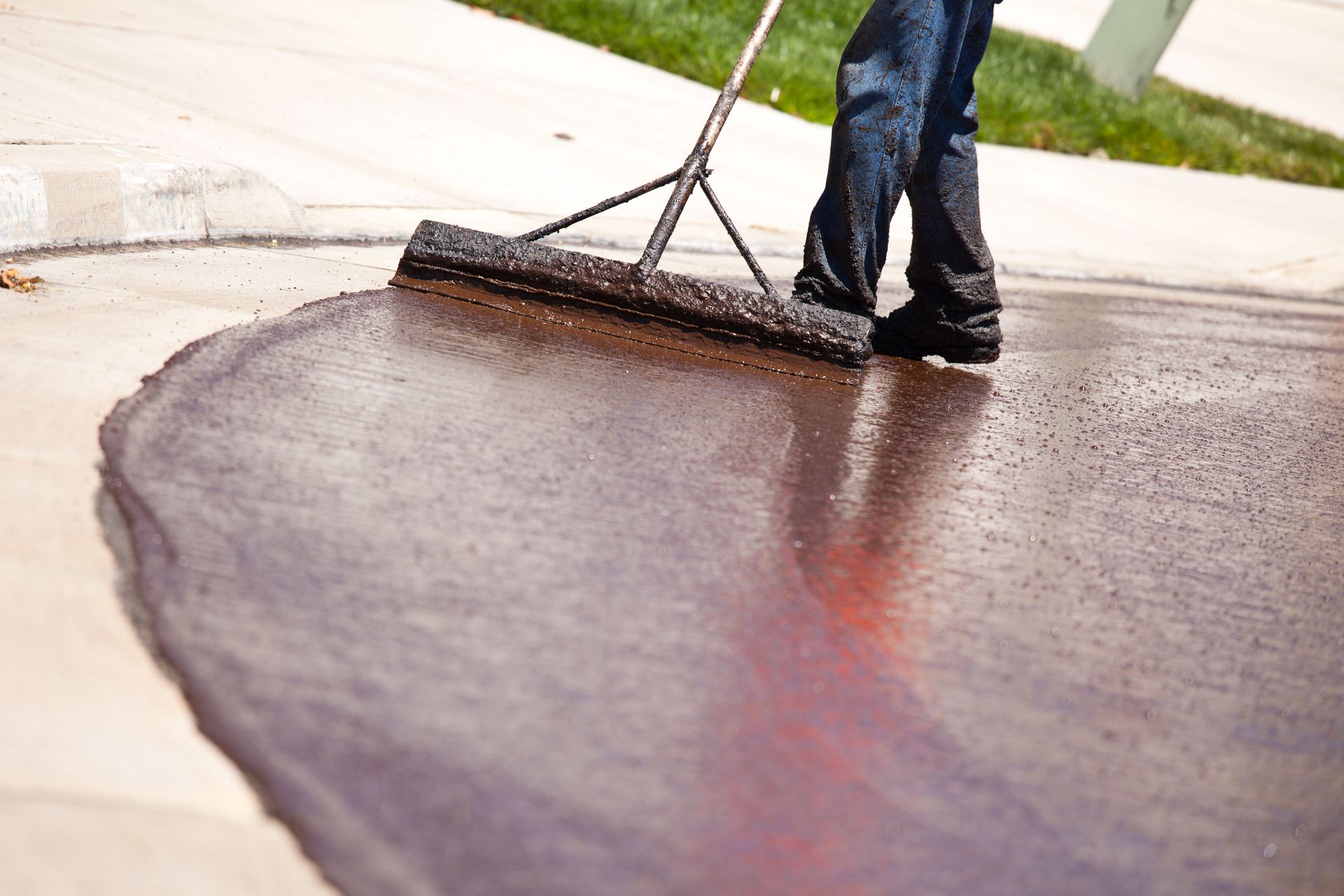 Person smoothing fresh dark asphalt with a rake on a driveway.