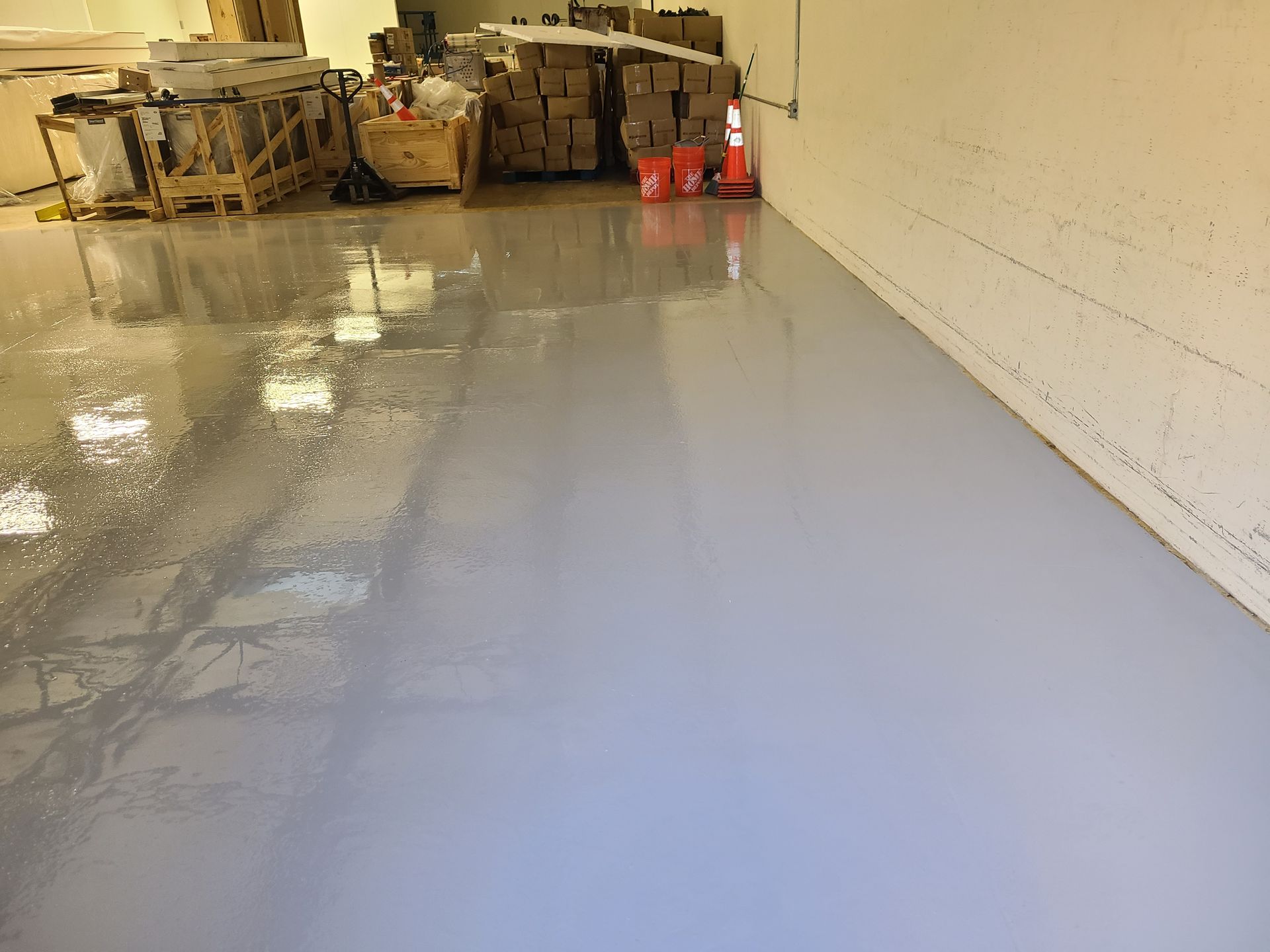 Glossy gray warehouse floor with storage pallets and orange cones along the back wall