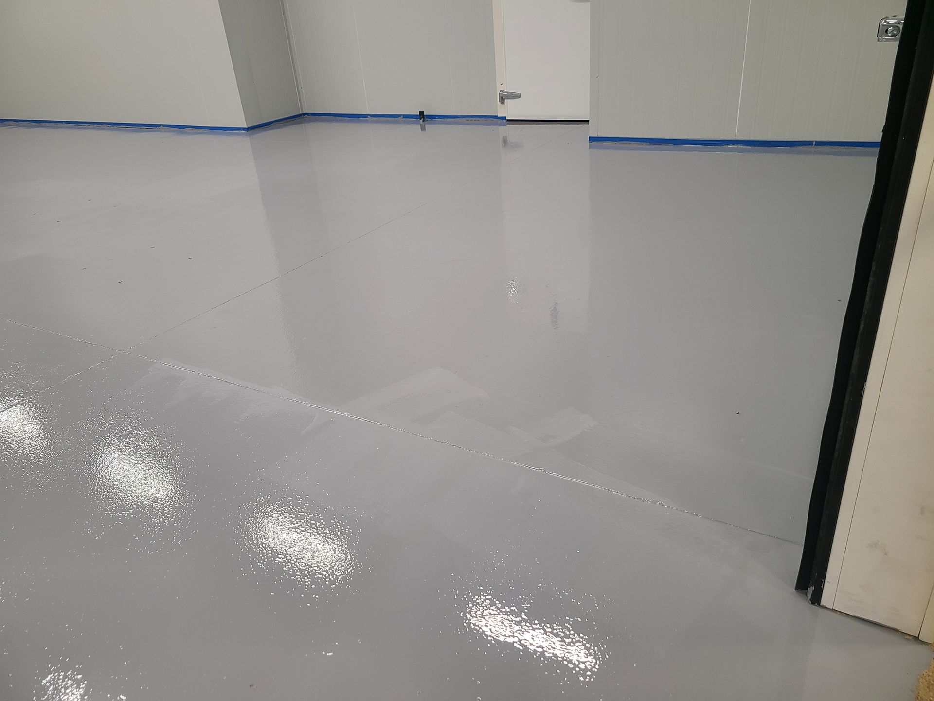 Empty room with glossy gray floor and white walls, partially taped-off doorway on the right