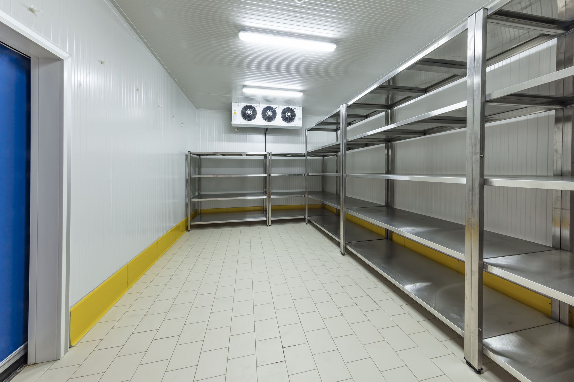 Empty refrigerated storage room with metal shelving, white walls, and tiled floor