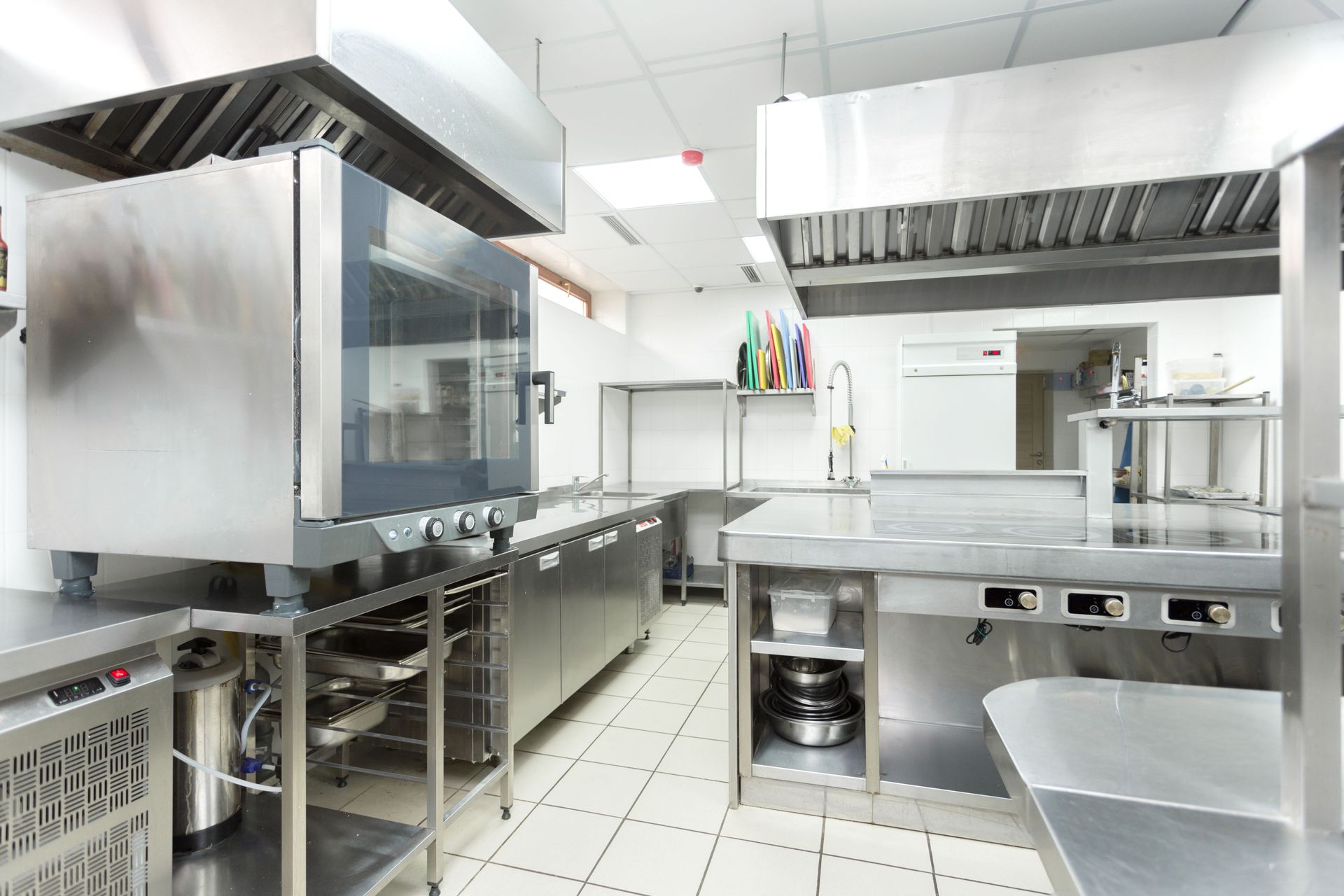 Bright stainless-steel commercial kitchen with counters, sinks, and cooking equipment