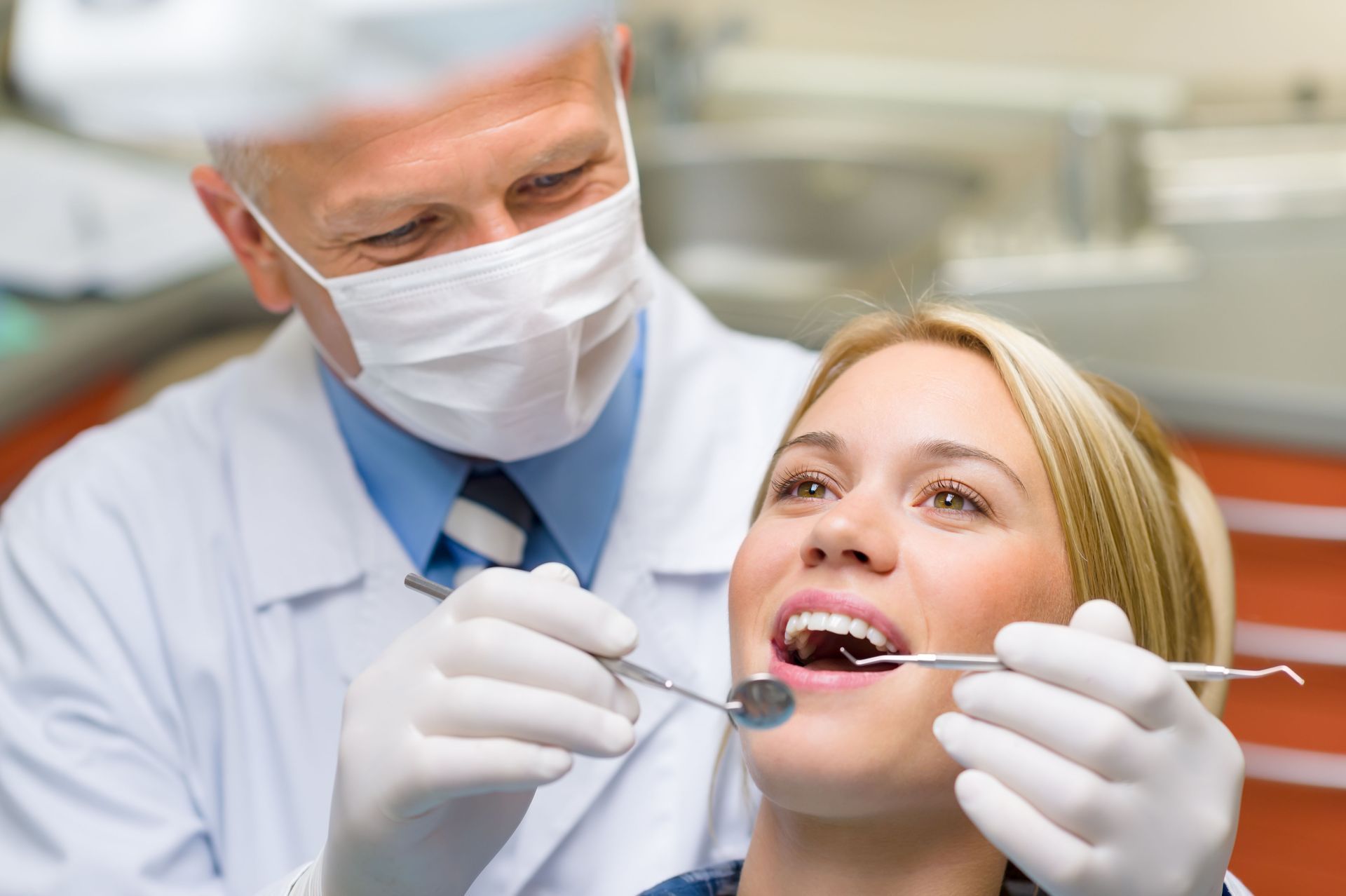 Dentist examining a smiling patient’s teeth with a mirror and probe in a clinic