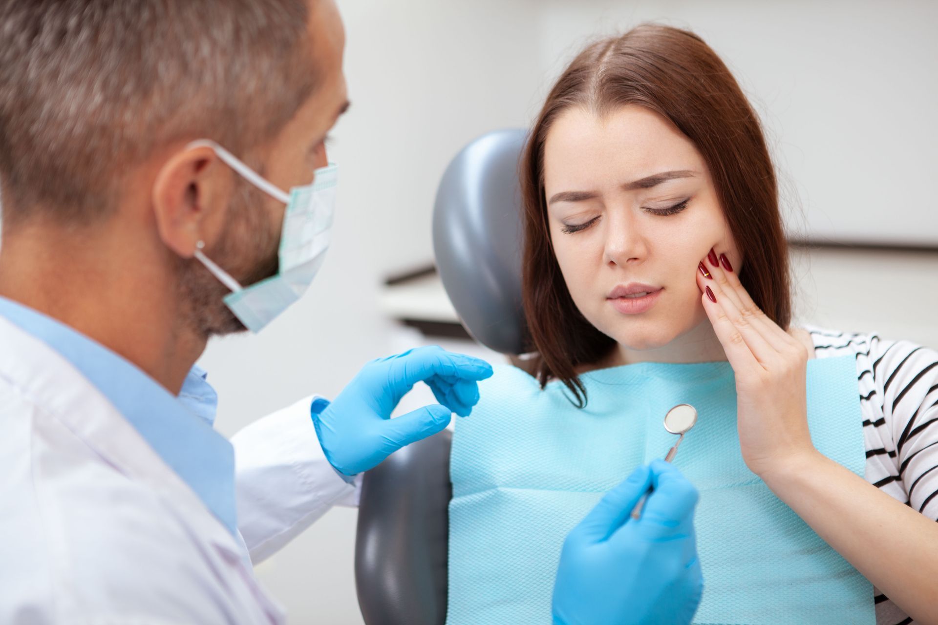 Dentist examining a patient with cheek pain in a dental chair, wearing blue gloves and mask