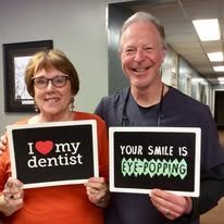 Two smiling people holding signs that say “I ♥ my dentist” and “Your smile is eye-popping”