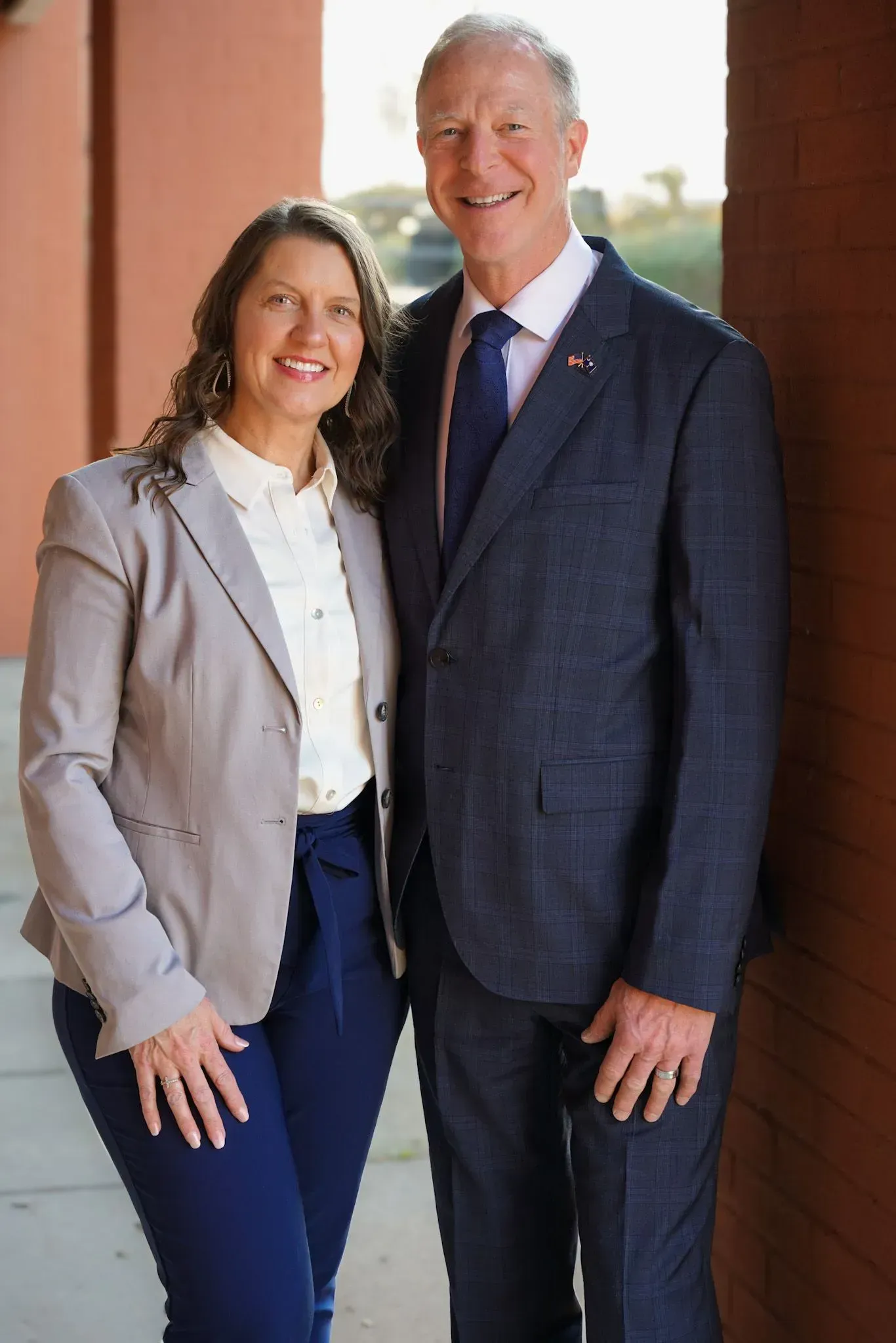 Two people standing together and smiling outdoors by a brick wall