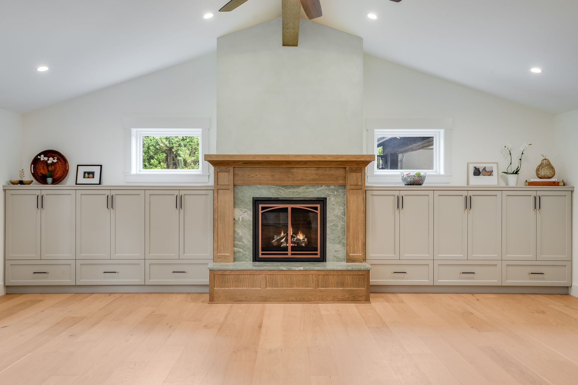 Living room with a fireplace flanked by built-in cabinets and small windows, light wood floors.