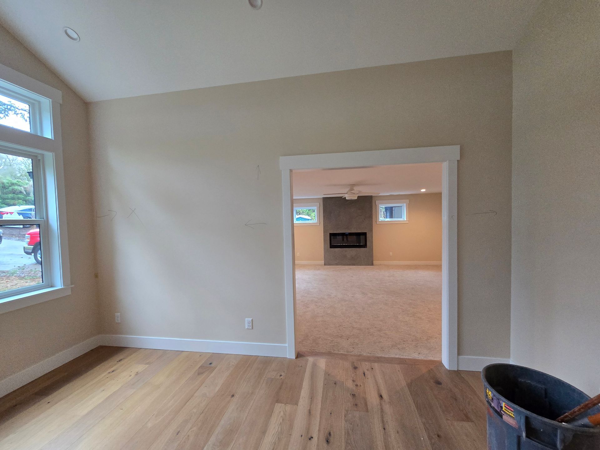 Interior view of a room with hardwood floors, a doorway to another room with a fireplace, and a window.