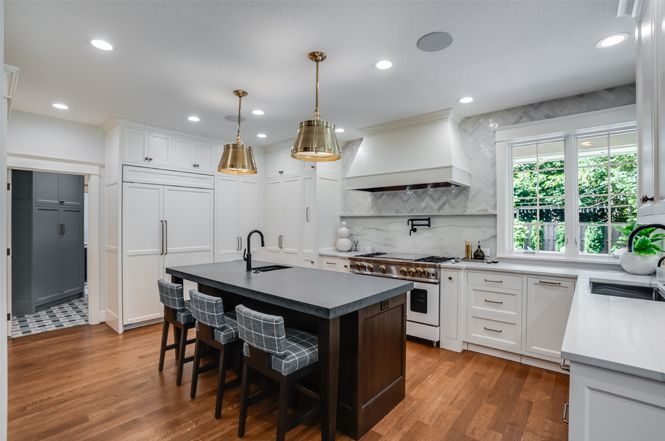 Modern kitchen with island, white cabinets, gold pendant lights, and hardwood floors.