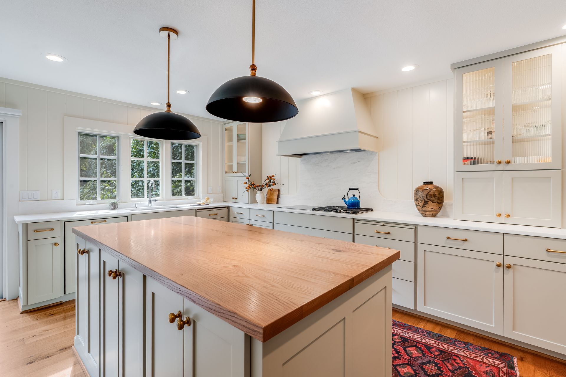 Kitchen with light grey cabinets, copper island countertop, black pendant lights, and large window.
