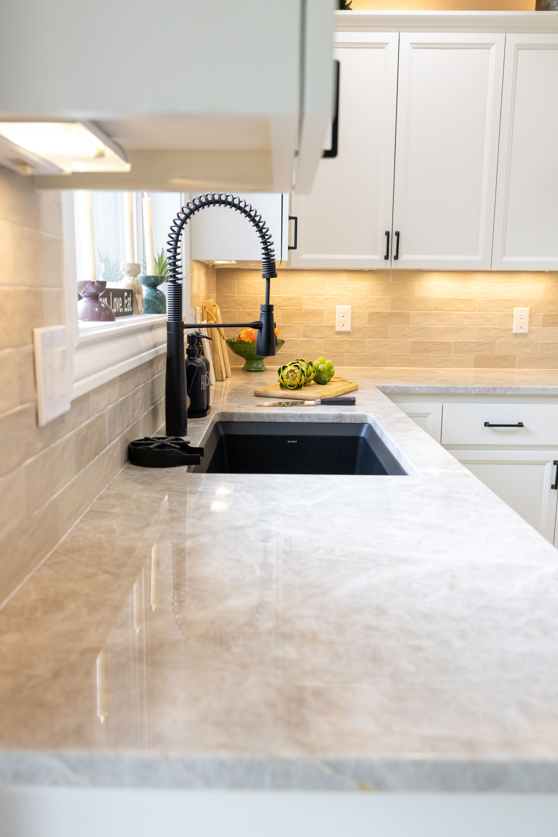 Kitchen countertop with black sink and faucet. White cabinets, tan backsplash.