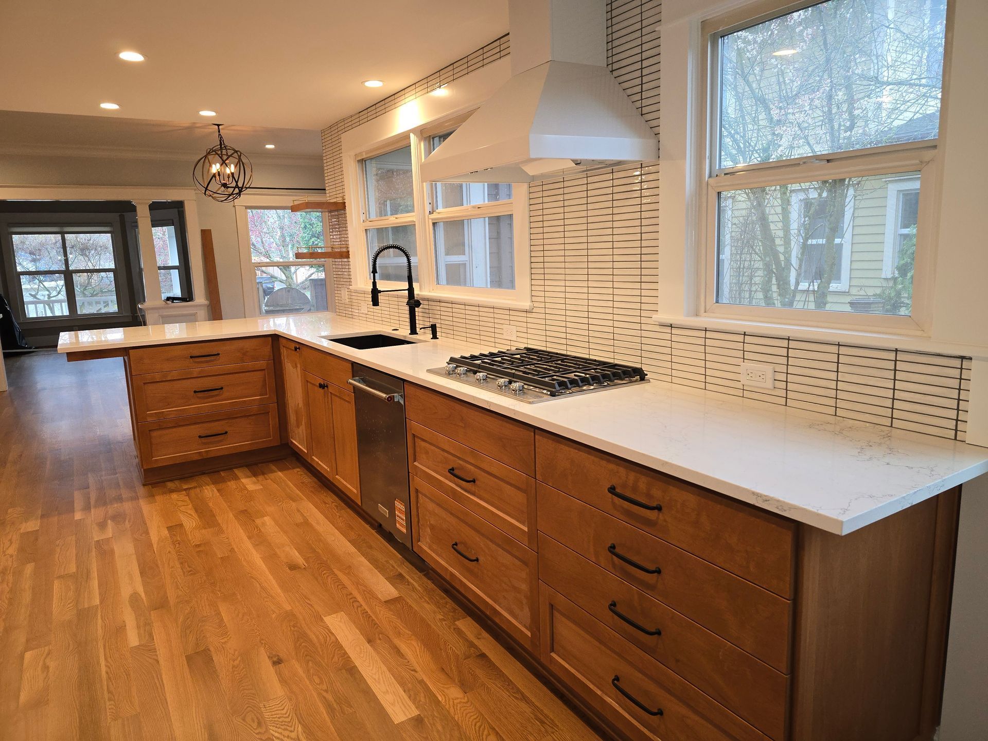 Modern kitchen with light wood cabinets, white countertops, and patterned backsplash.