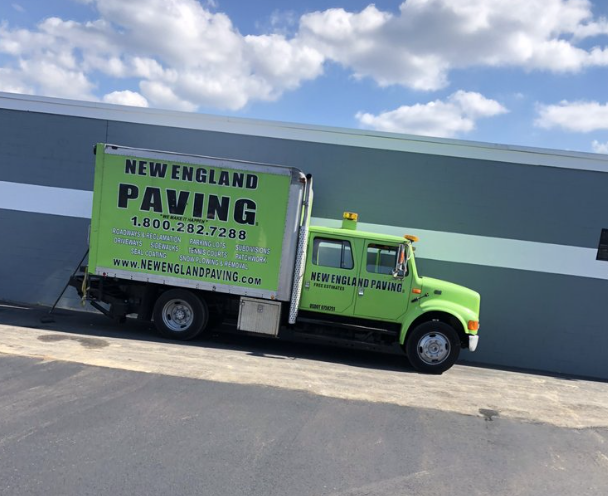 A green New England Paving truck is parked in front of a building