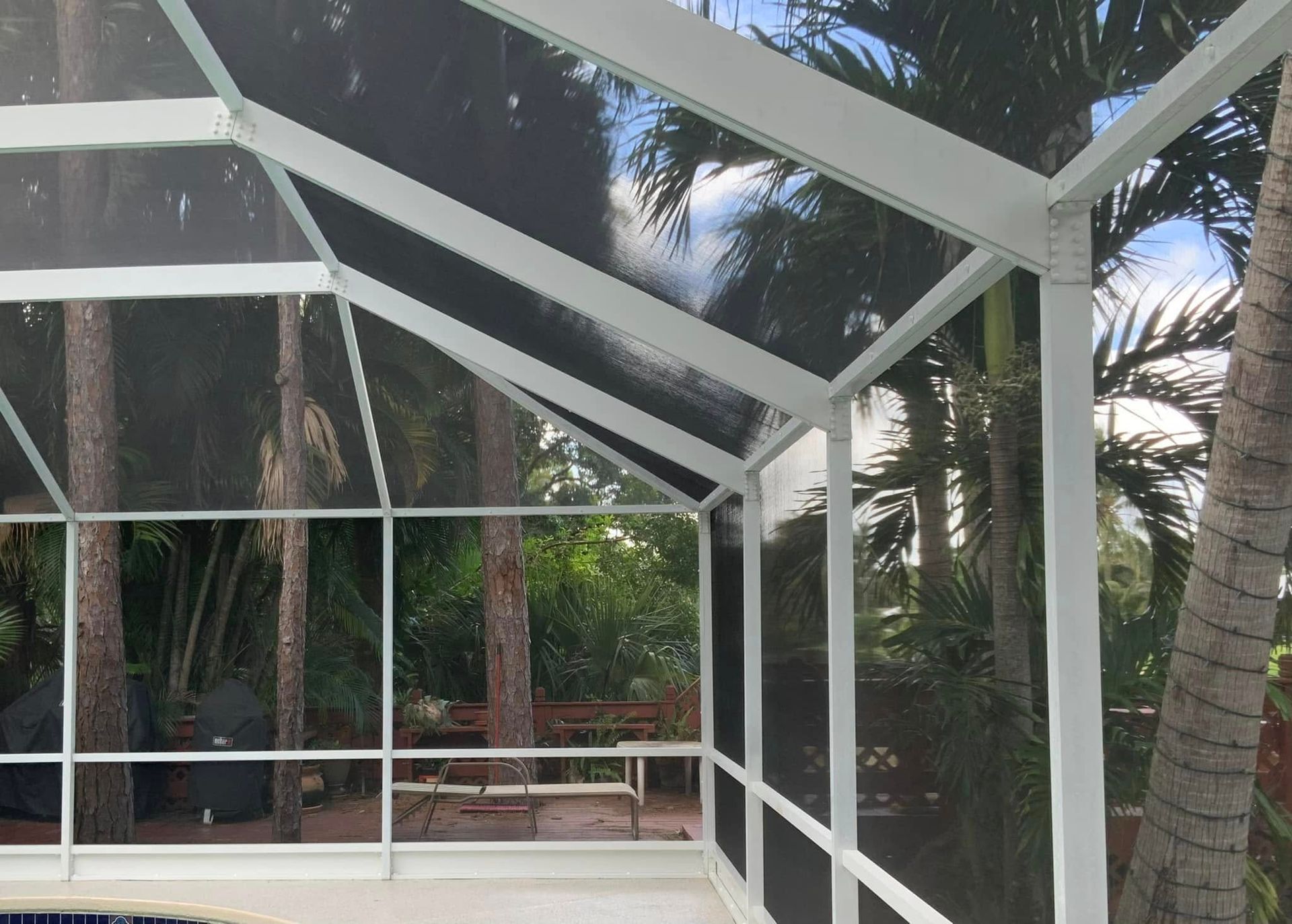 White screened-in patio enclosure with a view of trees and foliage.