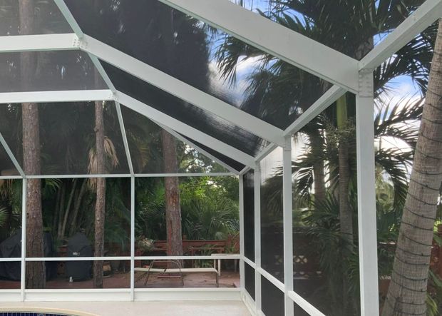 White screened-in patio enclosure with a view of trees and foliage.