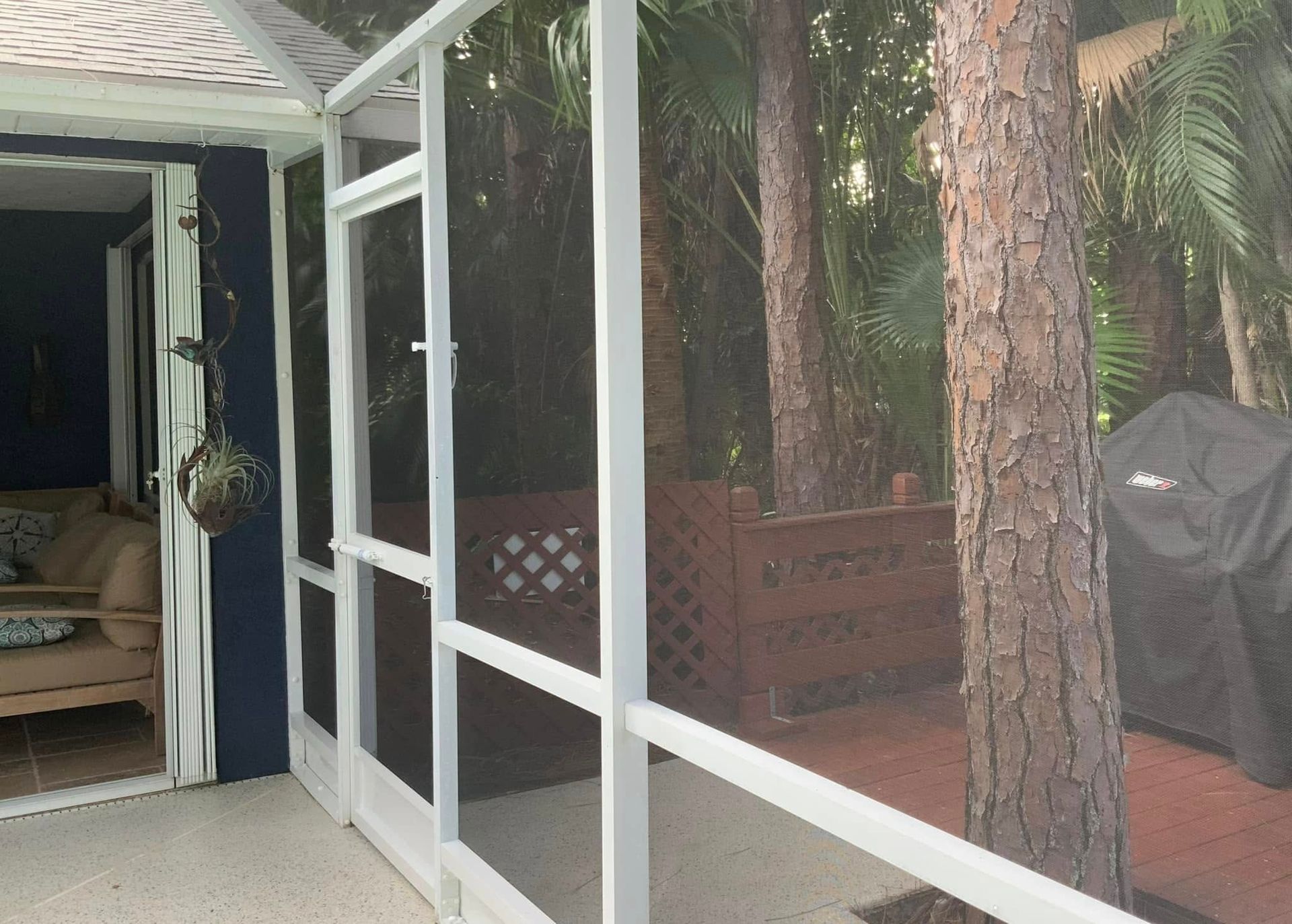 White screened-in patio overlooking a wooded backyard with a grill.