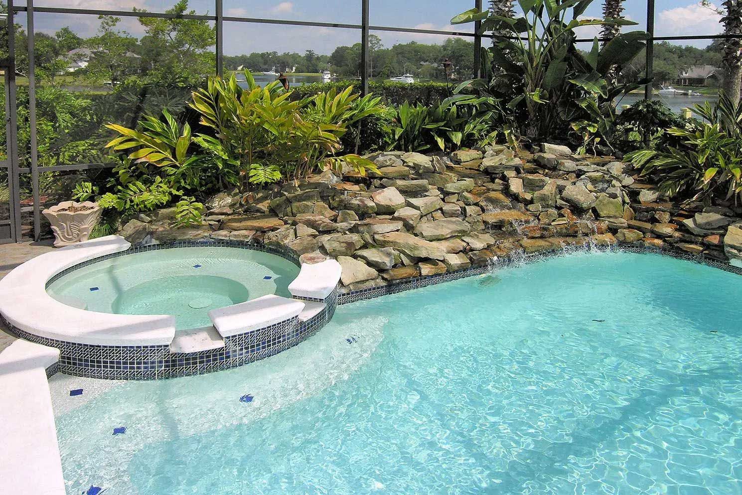 Swimming pool and hot tub with a rock waterfall and lush landscaping.