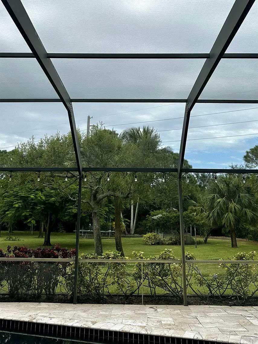 View through screened patio enclosure of a green yard with trees and cloudy sky.
