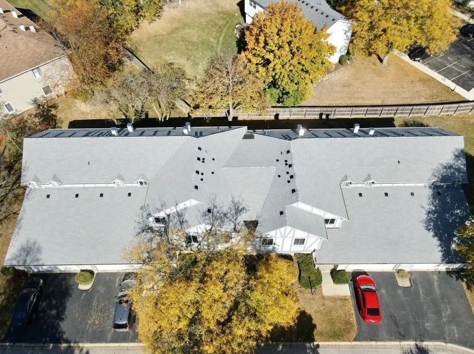 Aerial view of a gray-roofed apartment building with parking and autumn trees.