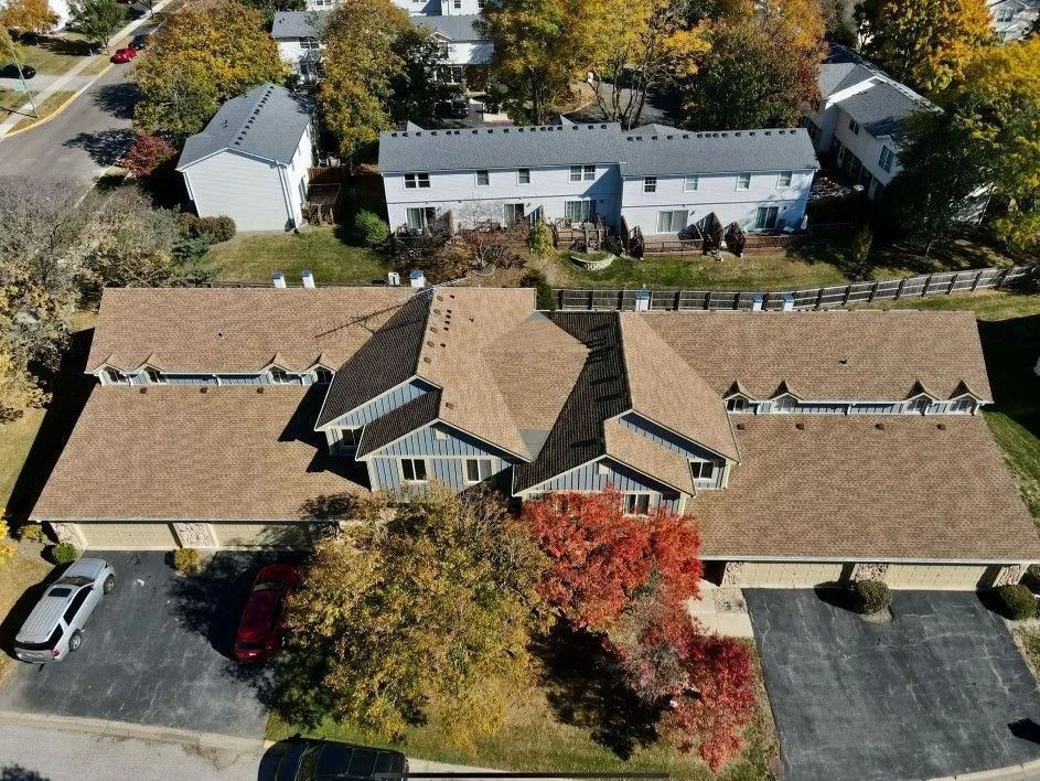 Aerial view of townhomes with brown roofs and driveways; fall foliage.