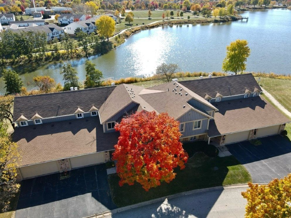 Aerial view of a building with a brown roof and colorful autumn tree in front of a lake.