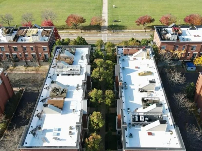 Overhead view of two long brick buildings with white roofs separated by a green courtyard with trees.