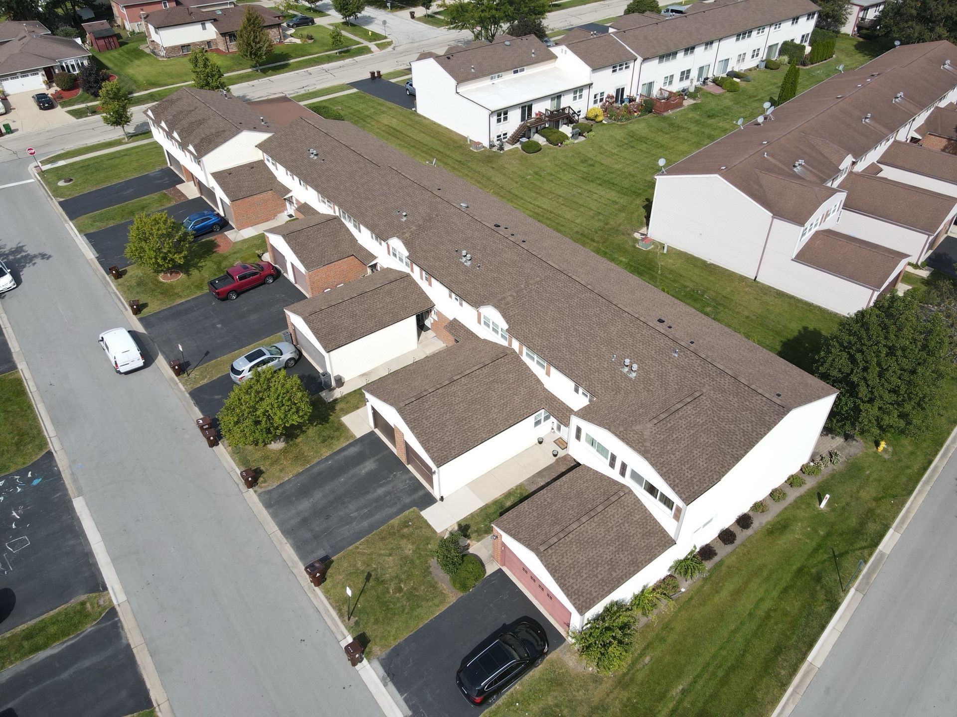 Aerial view of a row of townhouses with attached garages, brown roofs, and paved driveways.