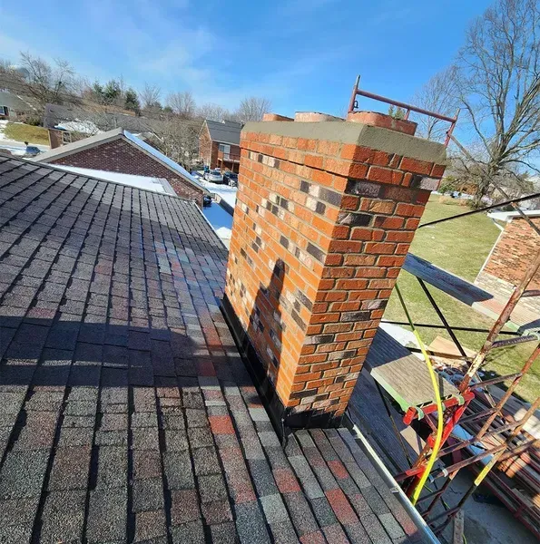 Brick chimney on a shingled roof with a clear blue sky.