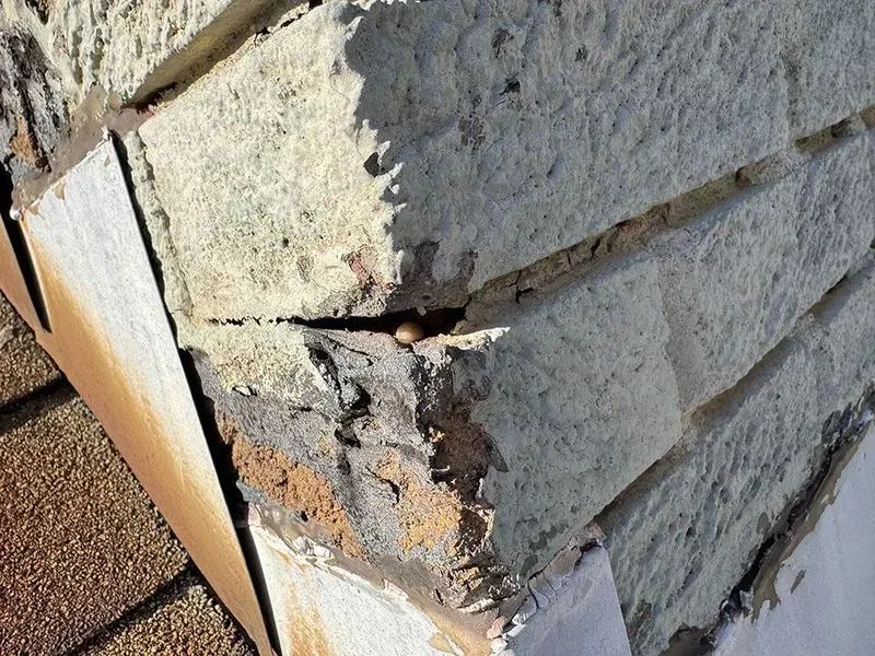 Close-up of damaged roof edge, showing crumbling stone blocks, cracked sealant, and exposed underlayment.