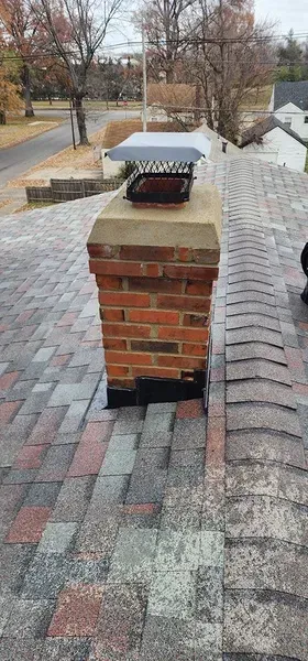 Brick chimney on a shingle roof with a chimney cap, overlooking a street with fall foliage.