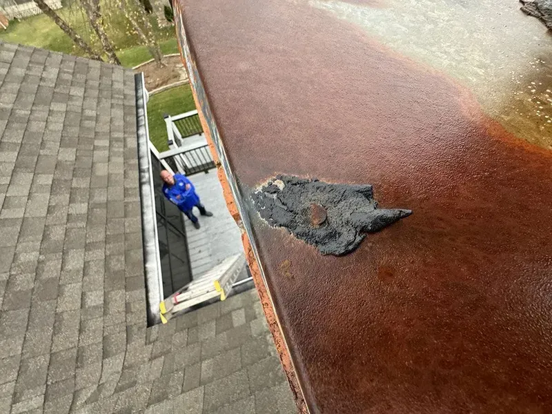 Man on roof near rusty edge and asphalt shingles.