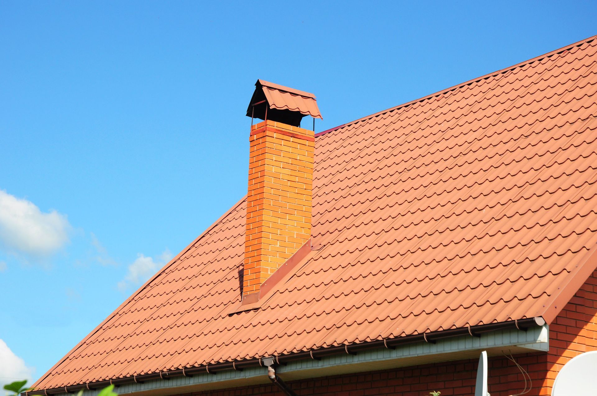 Red tiled roof with brick chimney against a blue sky.