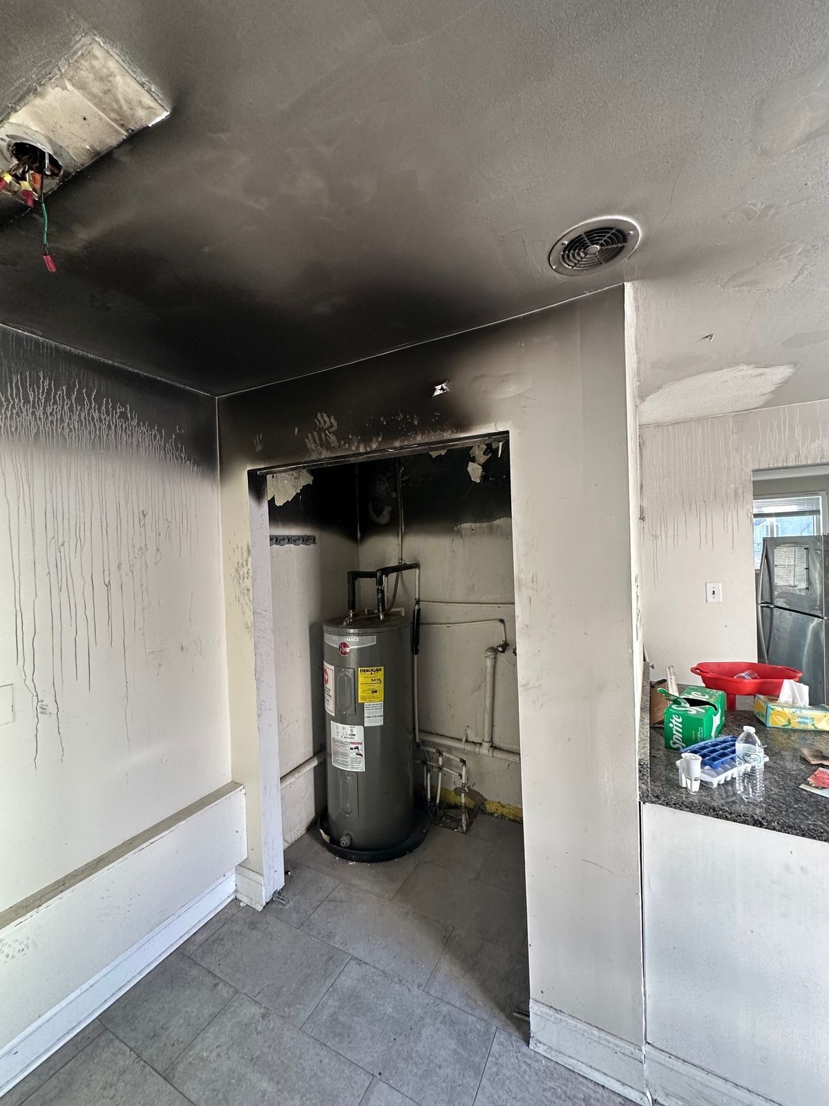 Charred kitchen interior, water heater in alcove, smoke damage on walls and ceiling.