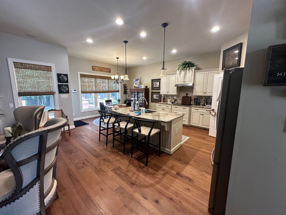 Spacious kitchen with island, white cabinets, and wood flooring. Includes bar stools, hanging lights, and windows with shades.