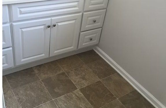 Bathroom with white cabinets, brown tile floor, and light gray wall.