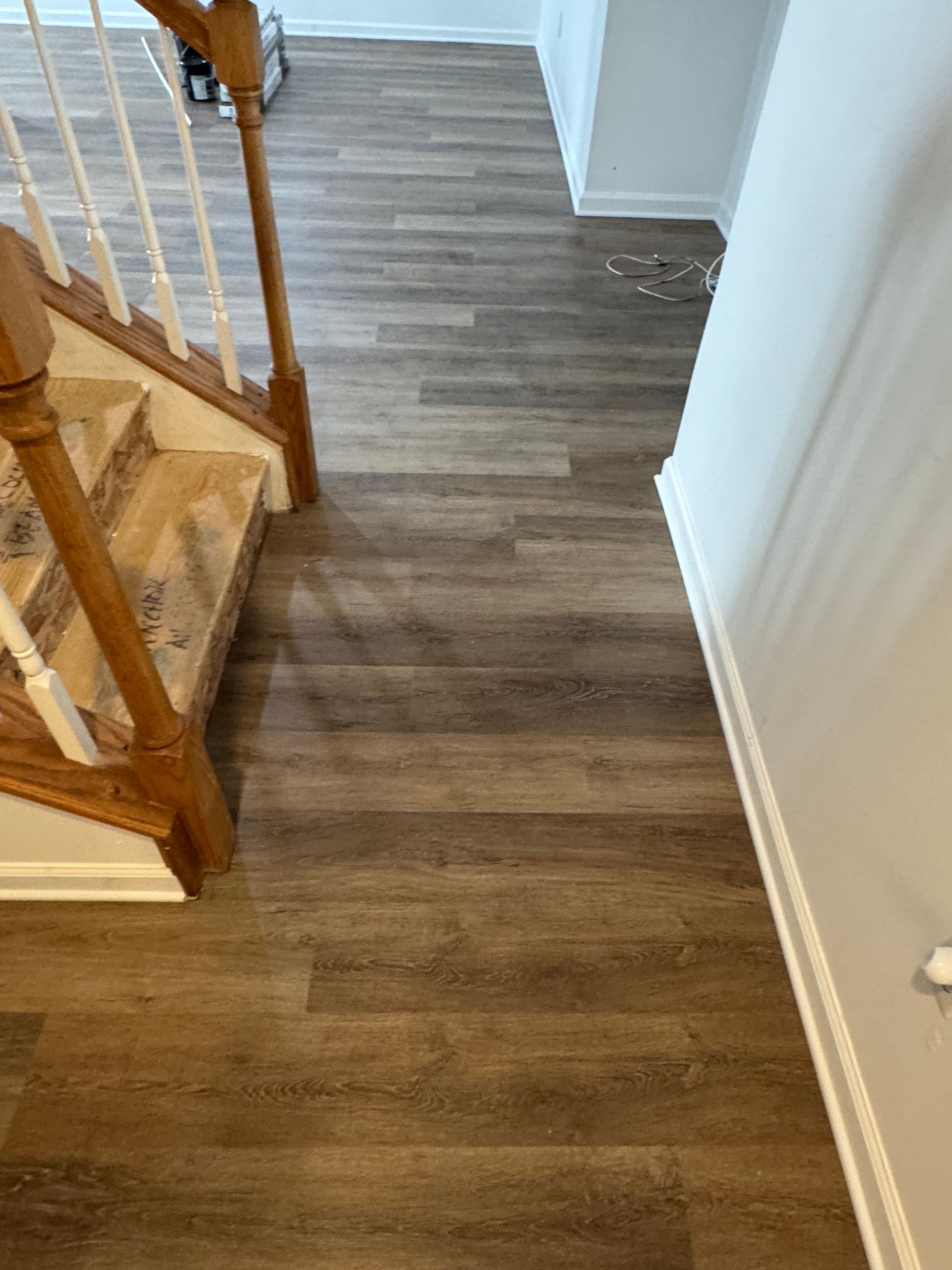 Wooden-look flooring in a hallway with stairs. Brown and beige tones.  A staircase with white banisters on the left.