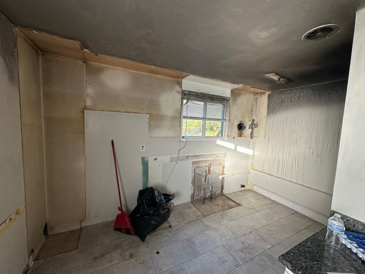 Kitchen gutted after a fire. Damaged walls, ceiling, and floor with debris.
