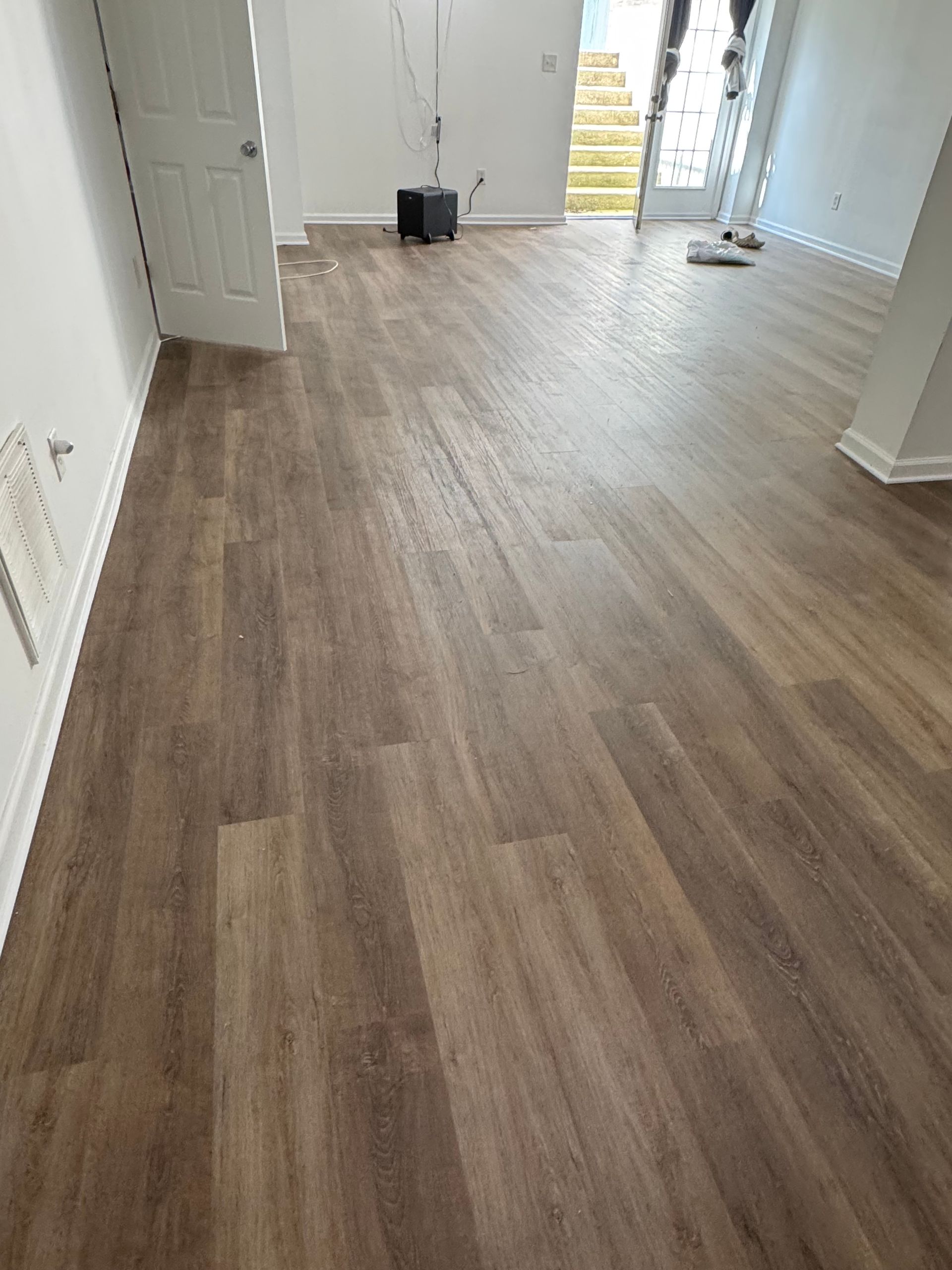 Hardwood-look flooring in a room with a white door, walls, and a glass door leading outside.