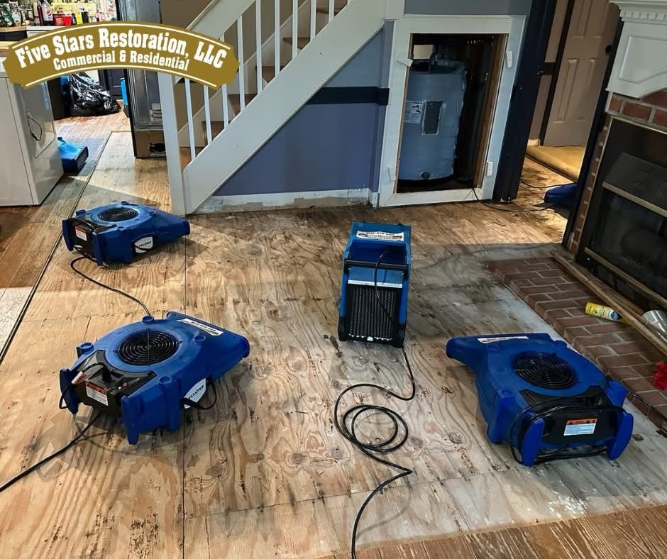 Dehumidifiers on plywood floor, near stairs and a water heater; restoration scene.