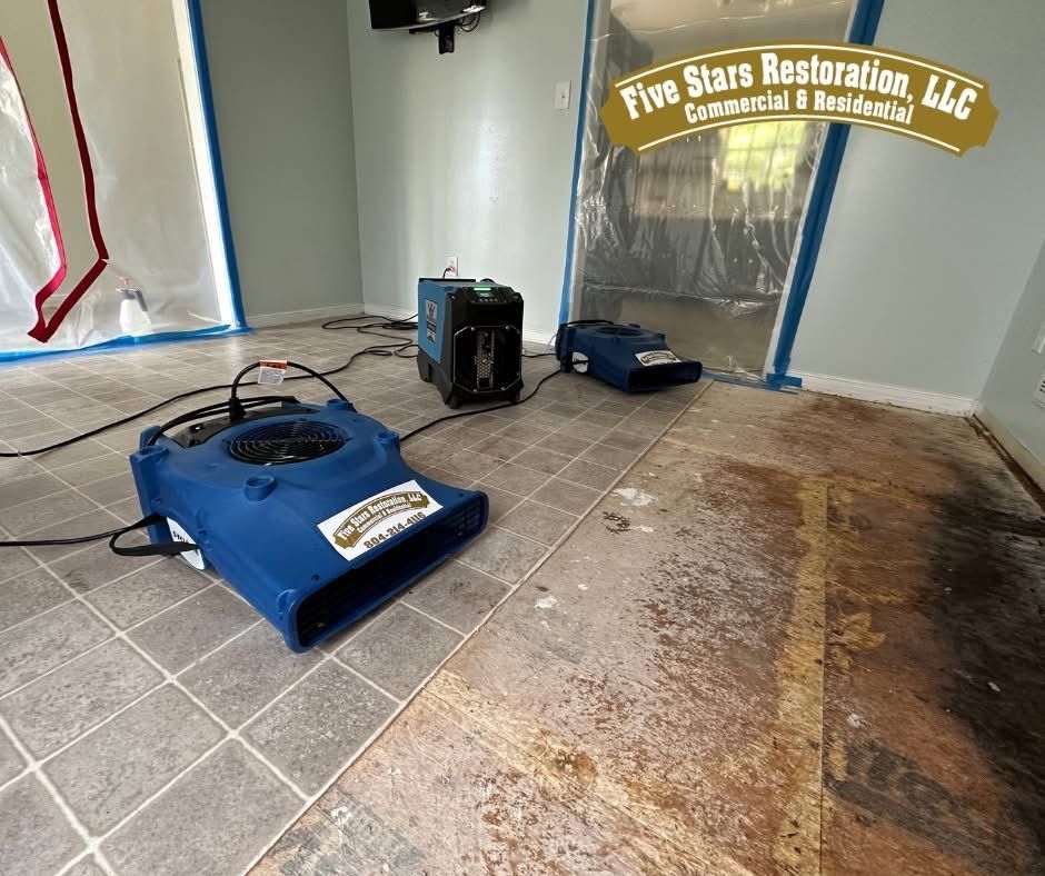 Two blue fans drying a room with water damage; plastic sheeting covers doorways.