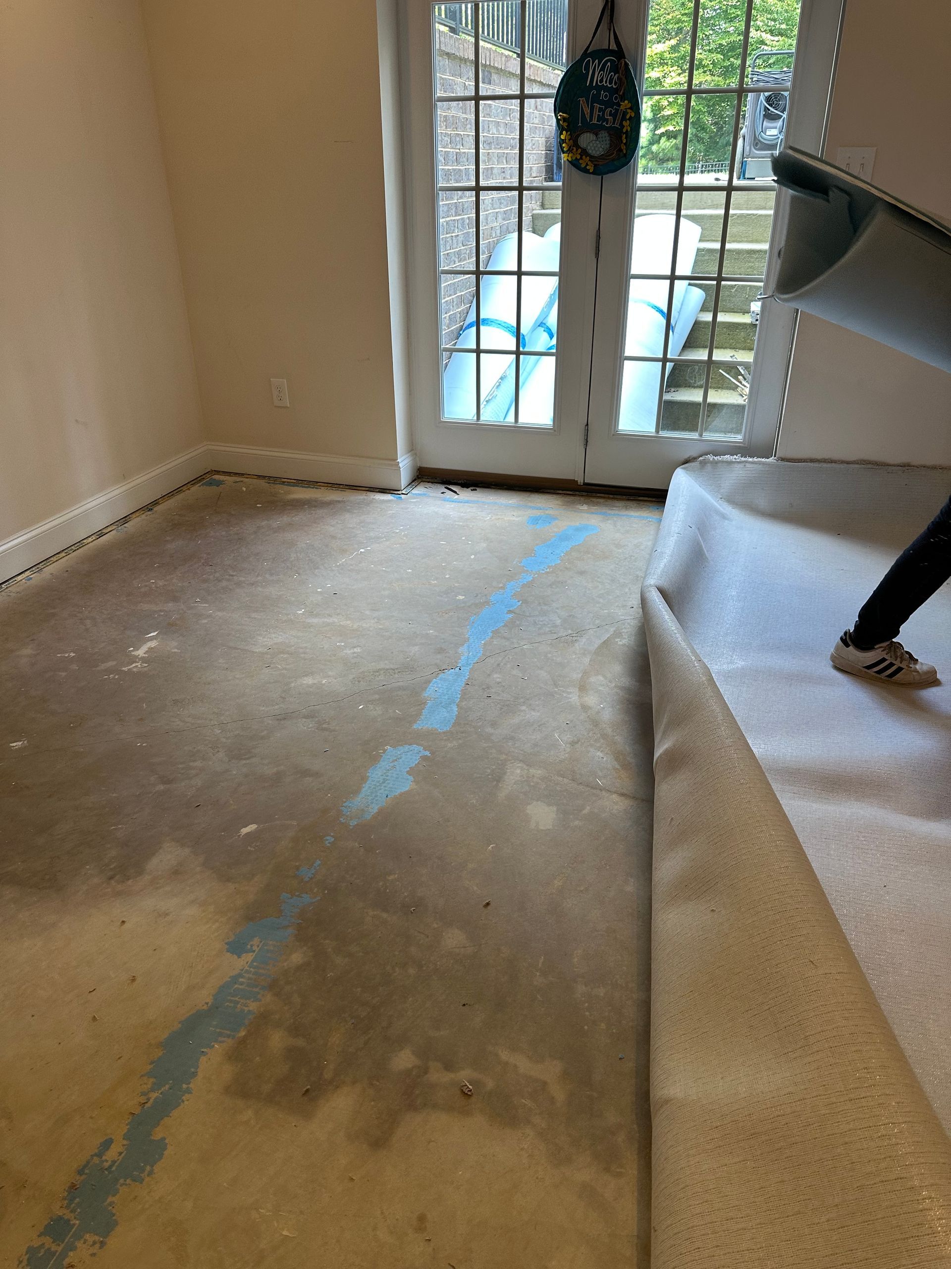 Bare concrete floor with a blue line, carpet being pulled up near a doorway.