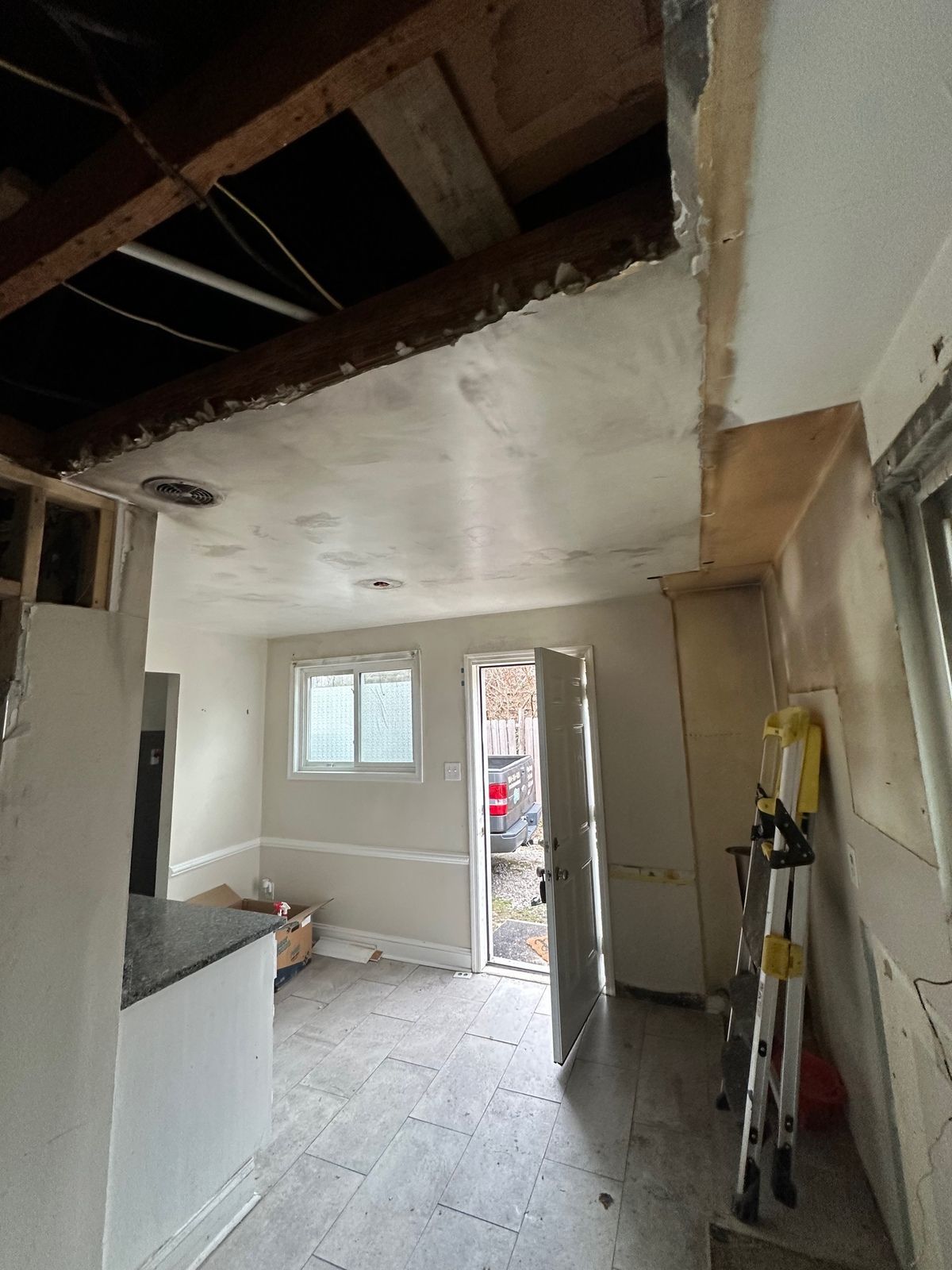Kitchen under construction, exposed ceiling beams, open doorway, unfinished walls, flooring.