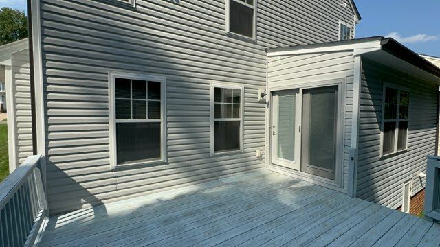 Back of a house with gray siding, white-trimmed windows and sliding door, and a white-painted wooden deck.