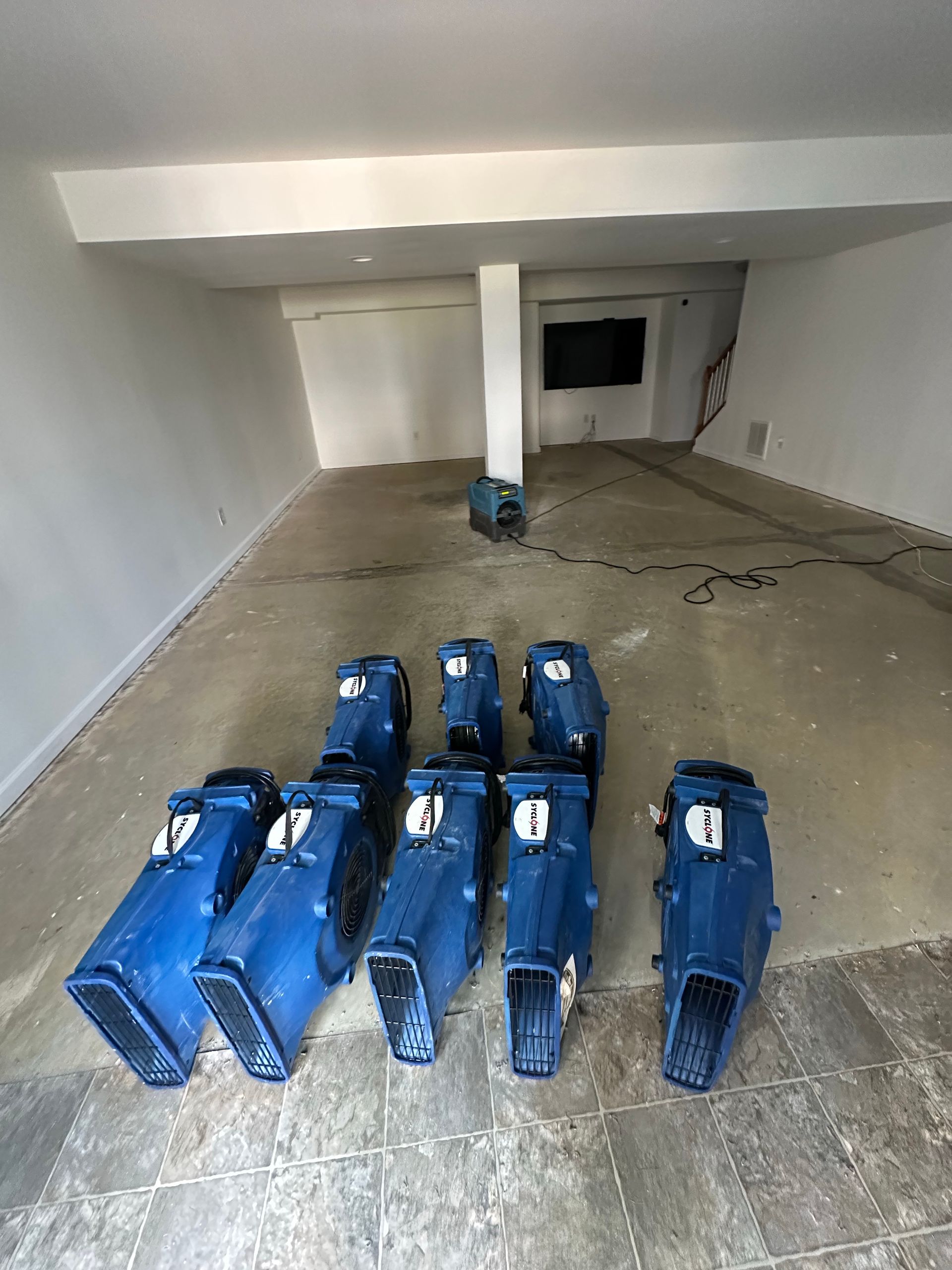 Blue containers are scattered on a concrete floor in a room with white walls and a large, dark screen.